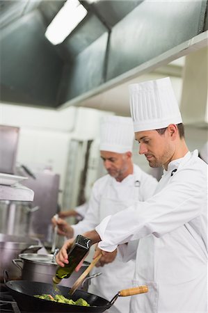 personnel career - Chef frying broccoli in a wok and adding olive oil Stock Photo - Premium Royalty-Free, Code: 6109-07601078