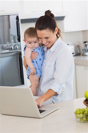 simsearch:6109-07601002,k - Mother using laptop while carrying baby at counter Photographie de stock - Premium Libres de Droits, Code: 6109-07601027