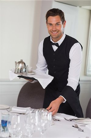 Happy waiter holding tray and setting table Stock Photo - Premium Royalty-Free, Code: 6109-07601183
