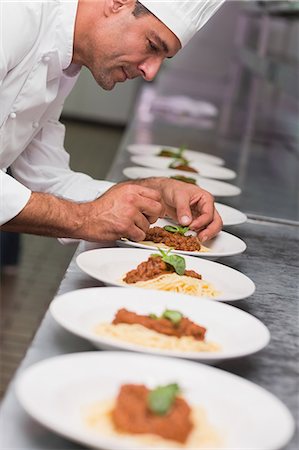 Happy chef putting basil leaf on spaghetti dish Foto de stock - Sin royalties Premium, Código: 6109-07601126