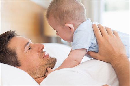 simsearch:6109-07601273,k - Father lying on bed with baby son in blue babygro Stock Photo - Premium Royalty-Free, Code: 6109-07601240