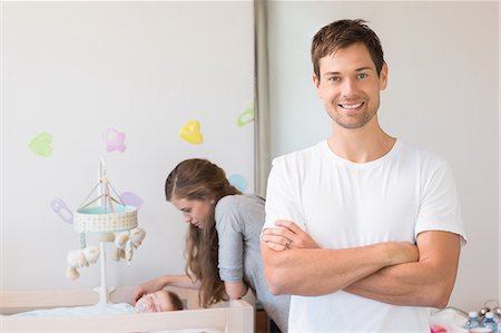 simsearch:6109-08945217,k - Happy mother watching over baby son in crib with father smiling at camera Fotografie stock - Premium Royalty-Free, Codice: 6109-07601294