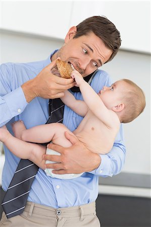 simsearch:614-01558935,k - Busy father holding his baby son before work and eating toast Foto de stock - Sin royalties Premium, Código: 6109-07601353