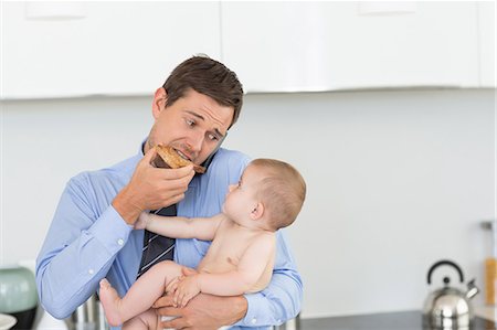 simsearch:6109-08536469,k - Busy father holding his baby son before work and eating toast Stock Photo - Premium Royalty-Free, Code: 6109-07601354