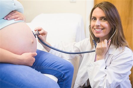 smiling doctor with stethoscope listening to pregnant lady - Smiling doctor checking a pregnant woman Stock Photo - Premium Royalty-Free, Code: 6109-08203373