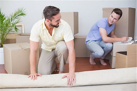 Handsome man unrolling carpet with his boyfriend behind Fotografie stock - Premium Royalty-Free, Codice: 6109-08203687