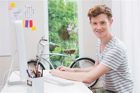 freelancer - Happy young man working at desk and looking at camera Stock Photo - Premium Royalty-Free, Code: 6109-08203754