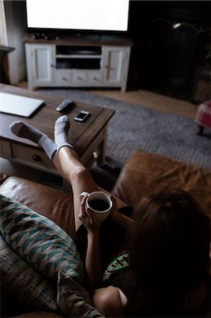 simsearch:6109-08390353,k - Young woman laying on the sofa holding mug Stock Photo - Premium Royalty-Free, Code: 6109-08390054