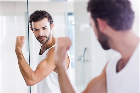 simsearch:6109-08435552,k - Smiling man looking at his biceps in mirror Fotografie stock - Premium Royalty-Free, Codice: 6109-08390433