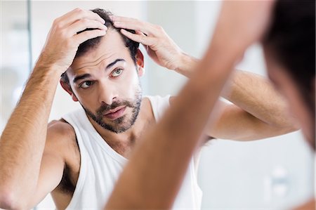 simsearch:6109-08435552,k - Concentrated man looking at his hair in mirror Fotografie stock - Premium Royalty-Free, Codice: 6109-08390435