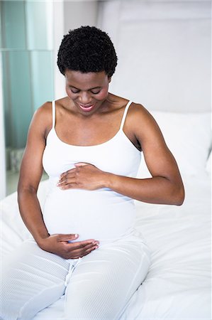 pregnant rubbing - Smiling pregnant woman sitting on her bed Stock Photo - Premium Royalty-Free, Code: 6109-08395281