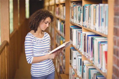 simsearch:400-08650429,k - Pretty student in library reading book Foto de stock - Royalty Free Premium, Número: 6109-08396600