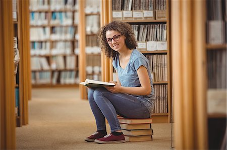 Pretty student in library sitting on books Stock Photo - Premium Royalty-Free, Code: 6109-08396626