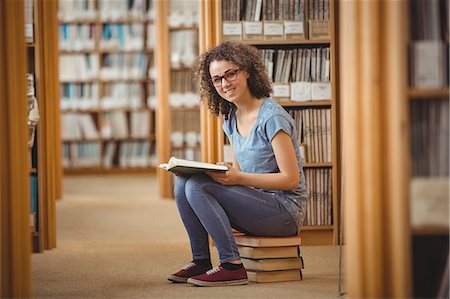 Pretty student in library sitting on books Photographie de stock - Premium Libres de Droits, Code: 6109-08396626