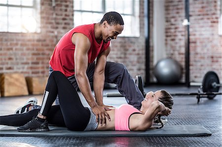 simsearch:6109-08397048,k - Male trainer assisting woman with abdominal crunches Photographie de stock - Premium Libres de Droits, Code: 6109-08397043