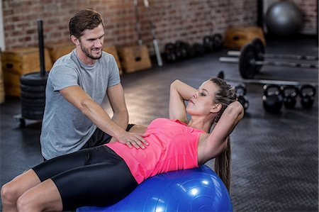 Trainer assisting woman with abdominal crunches Stock Photo - Premium Royalty-Free, Code: 6109-08397167