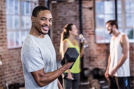 fitness class instructor - Smiling muscular man lifting a dumbbell Stock Photo - Premium Royalty-Free, Code: 6109-08397204