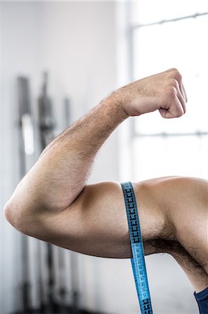 Impressive bicep on display. Muscular man measuring his bicep with a measuring  tape. Stock Photo by YuriArcursPeopleimages