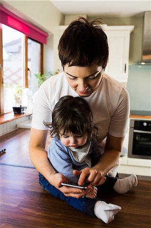 fond - Cute mother showing her phone to her baby in the kitchen Stock Photo - Premium Royalty-Free, Code: 6109-08481812