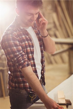 Happy carpenter on the phone in a dusty workshop Stock Photo - Premium Royalty-Free, Code: 6109-08481904