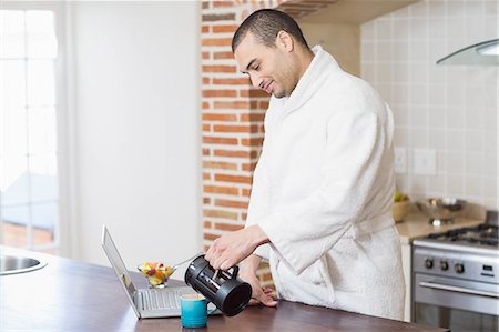 simsearch:6109-06781541,k - Smiling man drinking coffee and using laptop in the kitchen at home Stock Photo - Premium Royalty-Free, Code: 6109-08489030