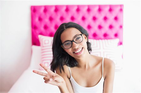 simsearch:6109-08489796,k - Brunette smiling sitting on a bed and making victory sign in a bedroom at home Photographie de stock - Premium Libres de Droits, Code: 6109-08489191