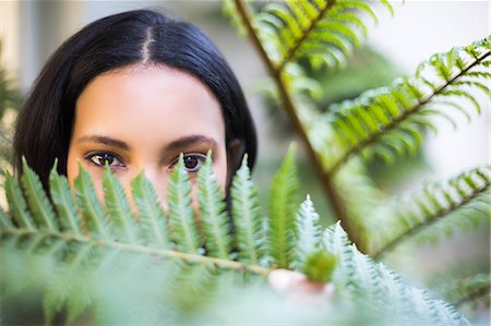 people hiding their face - Portrait of a pretty woman looking through leaves outside Stock Photo - Premium Royalty-Free, Code: 6109-08489232