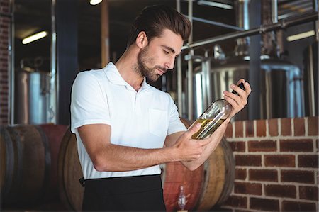 simsearch:6109-08489534,k - Winemaker examining bottle of white wine in a brewery Photographie de stock - Premium Libres de Droits, Code: 6109-08489532