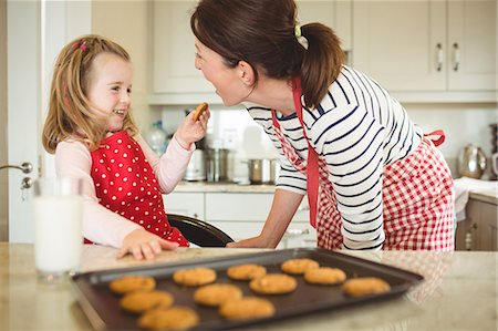 feliz - Daughter feeding cookie to mother in kitchen Foto de stock - Royalty Free Premium, Número: 6109-08434660