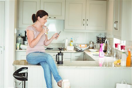 Woman sitting on the kitchen counter at home Stock Photo - Premium Royalty-Free, Code: 6109-08434712