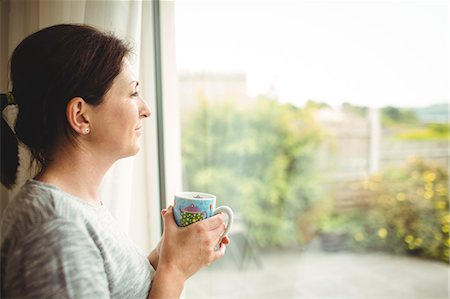 simsearch:6109-07496970,k - Portrait of woman with cup of coffee looking  through window Fotografie stock - Premium Royalty-Free, Codice: 6109-08434718