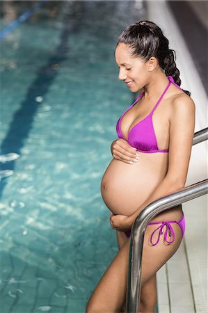 simsearch:6109-08435138,k - Smiling pregnant woman at the swimming pool touching her belly at the leisure center Foto de stock - Sin royalties Premium, Código: 6109-08435125