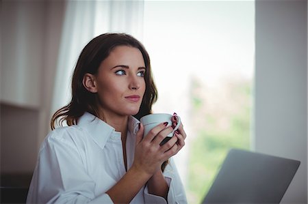 simsearch:6109-08390353,k - Thoughtful beautiful brunette using laptop while drinking coffee in the living room at home Stock Photo - Premium Royalty-Free, Code: 6109-08435571