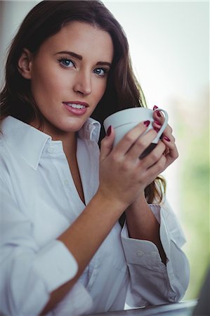 simsearch:6109-08390353,k - Thoughtful beautiful brunette using laptop while drinking coffee in the living room at home Stock Photo - Premium Royalty-Free, Code: 6109-08435572