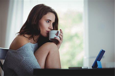 suéters - Thoughtful beautiful brunette using tablet while drinking coffee in the living room at home Foto de stock - Sin royalties Premium, Código: 6109-08435586
