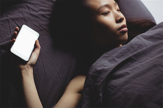 Brunette sleeping on the bed with smartphone at home Foto de stock - Sin royalties Premium, Código de la imagen: 6109-08435644