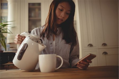 simsearch:6109-08435535,k - Brunette pouring water in her mug and using smartphone in the kitchen at home Stock Photo - Premium Royalty-Free, Code: 6109-08435665