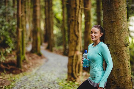 simsearch:6109-08435603,k - Fit brunette taking a break and holding bottle against a tree in the woods Stock Photo - Premium Royalty-Free, Code: 6109-08435615