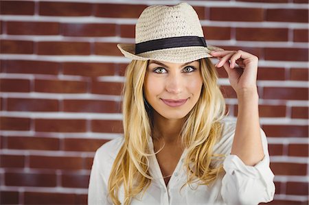 simsearch:6109-08398214,k - Beautiful blonde woman holding her hat against brick wall Photographie de stock - Premium Libres de Droits, Code: 6109-08435716