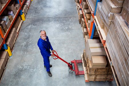 distribución - High angle view of man worker smiling with the pallet truck Stock Photo - Premium Royalty-Free, Code: 6109-08581611