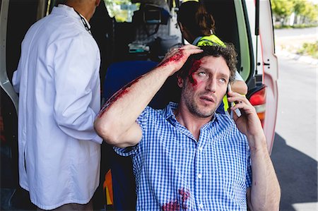 simsearch:6109-08581822,k - Injured man on the phone with ambulance men behind Stock Photo - Premium Royalty-Free, Code: 6109-08581808