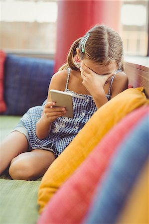 Upset girl sitting on sofa and holding a mobile phone Photographie de stock - Premium Libres de Droits, Code: 6109-08581946