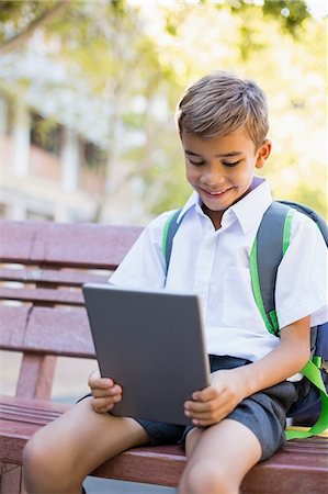 Schoolboy sitting on bench and using digital tablet in campus Stock Photo - Premium Royalty-Free, Code: 6109-08581951