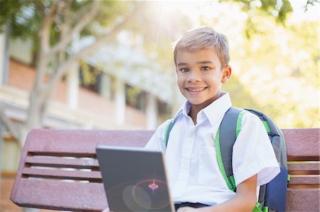 Happy schoolboy sitting on bench with digital tablet Foto de stock - Sin royalties Premium, Código: 6109-08581952