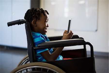 Disabled schoolboy on wheelchair using digital tablet Stock Photo - Premium Royalty-Free, Code: 6109-08581936