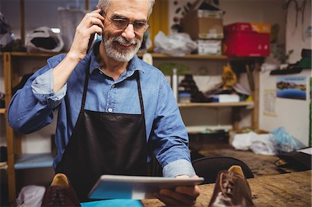 Cobbler calling with his mobile phone and holding a tablet computer Stock Photo - Premium Royalty-Free, Code: 6109-08582167