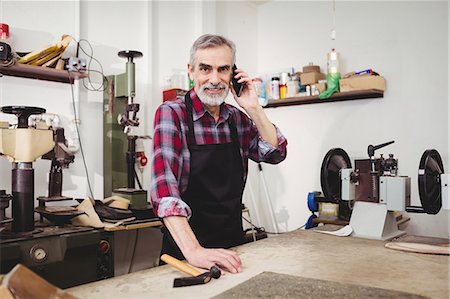 Cobbler smiling and calling with his mobile phone Stock Photo - Premium Royalty-Free, Code: 6109-08582180