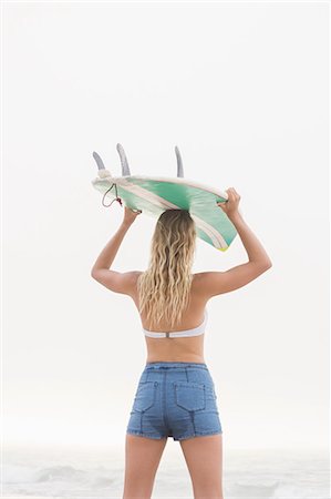 simsearch:6109-08536861,k - Pretty blonde woman holding a surfboard over her head Foto de stock - Sin royalties Premium, Código: 6109-08536859