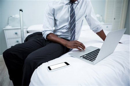 simsearch:6109-08537097,k - Mid-section of man sitting on bed and using laptop Stock Photo - Premium Royalty-Free, Code: 6109-08537145