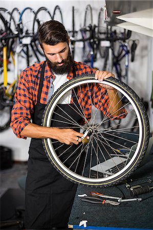 simsearch:6109-08537274,k - Hipster bike mechanic holding a bike wheel Stock Photo - Premium Royalty-Free, Code: 6109-08537302